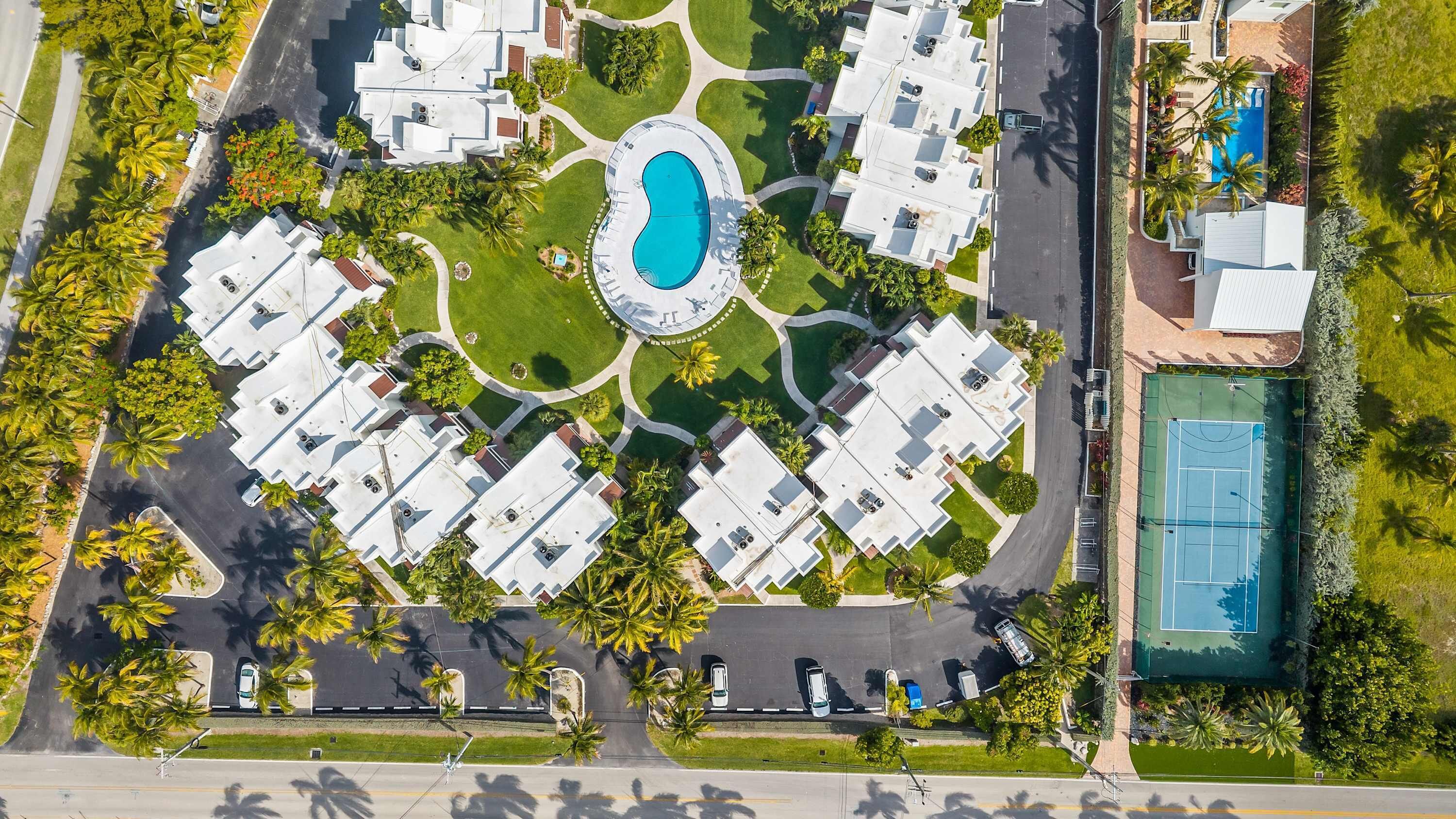 Luchtbeeld van een wooncomplex met een centraal gelegen zwembad, meerdere appartementencomplexen en een tennisbaan.
