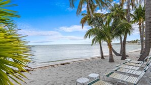 Ein Strand mit weißen Liegestühlen und Palmen.