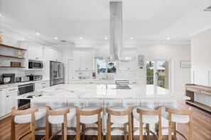 Una cocina moderna con armarios blancos, una isla grande con taburetes altos, electrodomésticos de acero inoxidable y vistas al exterior.