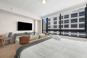 Ein modernes Hotelzimmer mit einem großen Bett, einem Schreibtisch, einem Flachbildfernseher und Blick auf ein Gebäude durch das Fenster.