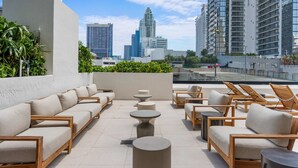 Una terraza en la azotea con asientos al aire libre, vistas de edificios de la ciudad y un cielo despejado.