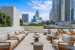 Eine Dachterrasse mit Sitzgelegenheiten im Freien, Blick auf Stadtgebäude und einen klaren Himmel.
