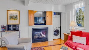 Una sala de estar con chimenea, un sofá, un diván rojo, un televisor y una lavadora.