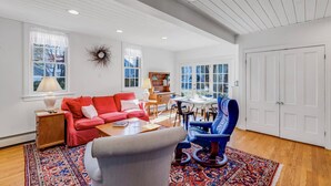 Un salón amplio con un sofá rojo, un sillón azul, una mesa de centro de madera y una alfombra estampada.