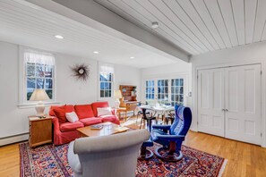 A spacious living room with a red sofa, a blue armchair, a wooden coffee table, and a patterned rug.