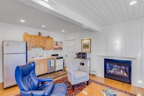 A living room with a fireplace, a kitchen area, and a blue leather chair.
