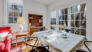 A dining area with a table set for four, a red chair, a wooden bookshelf, and a window with a view of trees.
