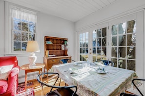 A dining area with a table set for four, a red chair, a wooden bookshelf, and a window with a view of trees.