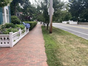 Ein Pflasterweg aus Ziegelsteinen mit weißem Zaun, einer Straße und Bäumen.