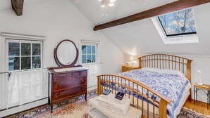 A bedroom with a wooden bed, a dresser, a mirror, a ceiling fan, and a skylight.