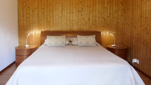 Une chambre à coucher avec une tête de lit en bois, un grand lit avec une literie blanche, deux tables de chevet et une lampe fixée au mur.