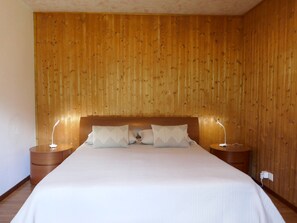 Un dormitorio con cabecera de madera, una cama grande con ropa de cama blanca, dos mesitas de noche y una lámpara de pared.