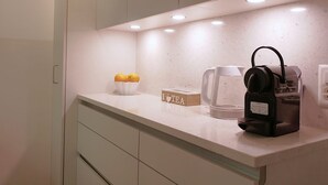 Une cuisine équipée d’une machine à café, d’une bouilloire et d’un saladier rempli de citrons, posés sur le plan de travail.