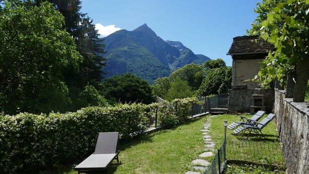 Un jardin avec un chemin en pierre, un fauteuil de relaxation et un bâtiment doté d’un mur en pierre.
