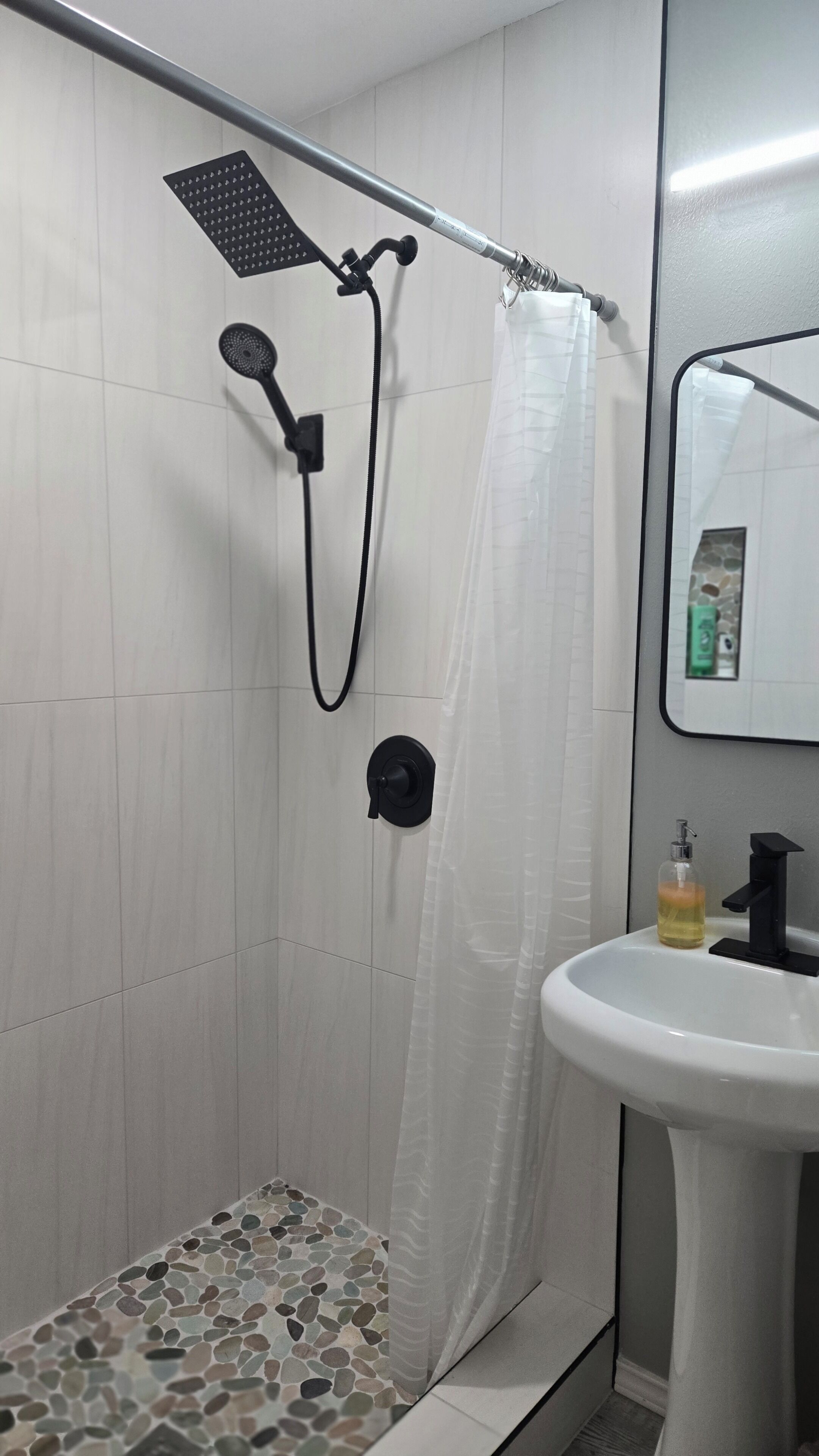 Ducha con cabezal de ducha de mano, pomo de control negro y cortina de ducha blanca.