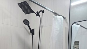 Doccia con soffione a mano, manopola di controllo nera e tenda da doccia bianca.