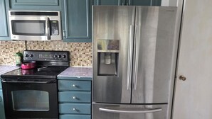 In cucina, un frigorifero in acciaio inossidabile, un forno a microonde e un piano cottura, con pensili color acquamarina e zoccolo piastrellato.