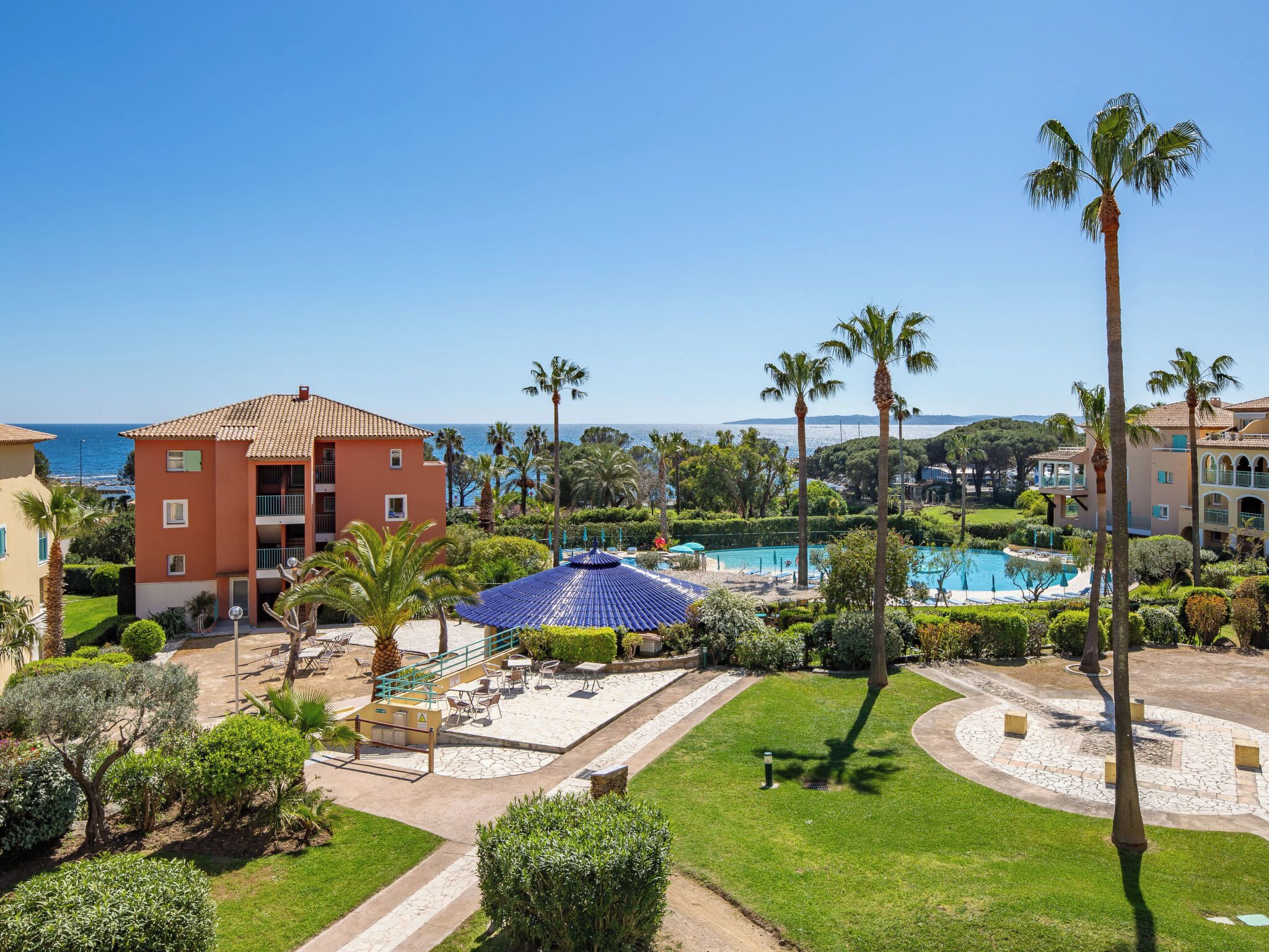 A resort with a swimming pool, palm trees, and a view of the sea.