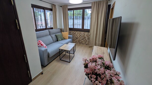 Ein Wohnzimmer mit einer Couch, einem Couchtisch, einem Fernseher und einem Fenster mit Vorhängen.