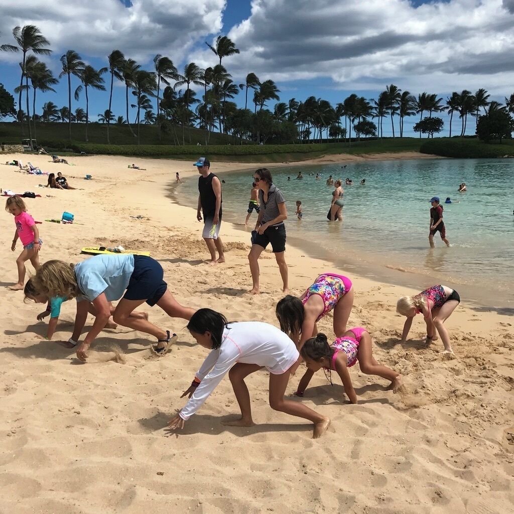 A beach with palm trees, people sunbathing, and children playing in the sand.