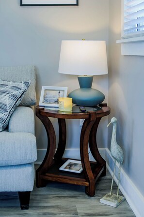 Esquina de una habitación con una lámpara azul sobre una mesa de madera, un cuadro enmarco, una vela y una escultura decorativa de un pájaro.