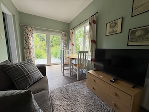 A living room with a sofa, TV, wooden dresser, and a dining table with chairs.