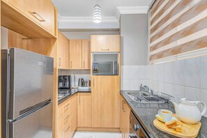 Cozinha moderna com armários de madeira, eletrodomésticos de aço inoxidável, micro-ondas, chaleira e espaço para café.