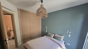 Ein Schlafzimmer mit einem Bett, einer Tür, einem Kleiderschrank und einer Pendelleuchte.