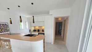 Eine moderne Küche mit Kochinsel, Pendelleuchten und Blick in das angrenzende Schlafzimmer.