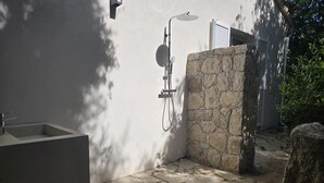 Ein Outdoor-Duschbereich mit Steinwänden, integriertem Waschbecken, Steinpflasterung und viel Grün.