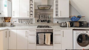 Una cocina moderna con armarios blancos, horno empotrado, microondas y lavadora.