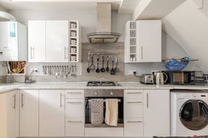 Una cocina moderna con armarios blancos, horno empotrado, microondas y lavadora.