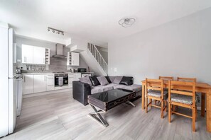 A modern kitchen with white cabinets, a dining area with a glass coffee table and wooden chairs, and a staircase leading to an upper level.