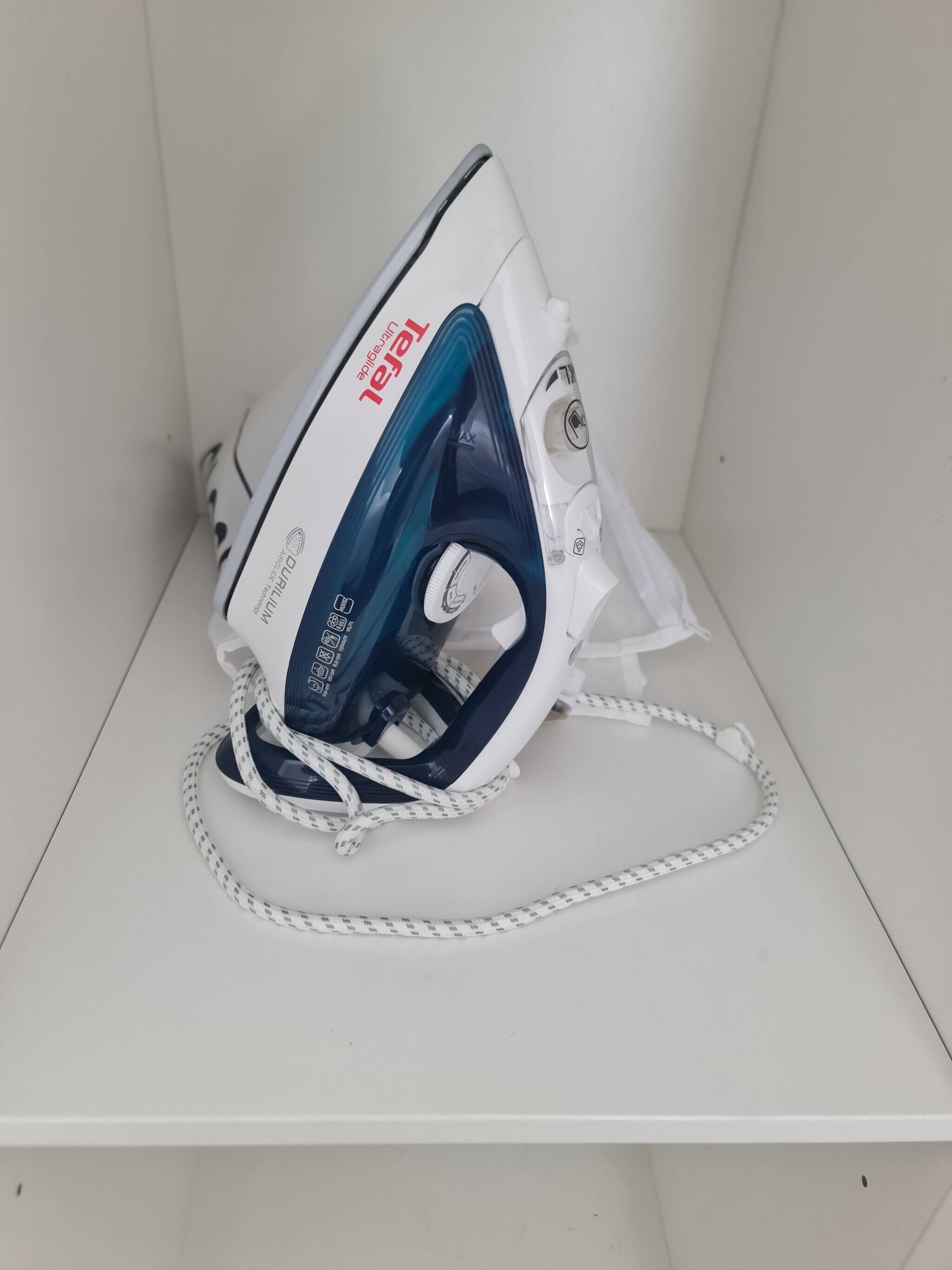 An iron with a cord, placed on a white surface.