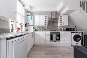 Una cocina moderna con armarios blancos, lavavajillas, lavadora y horno empotrado.