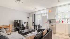 Una sala de estar moderna con sofá, mesa de centro, televisor y área de cocina con lavavajillas y armarios.