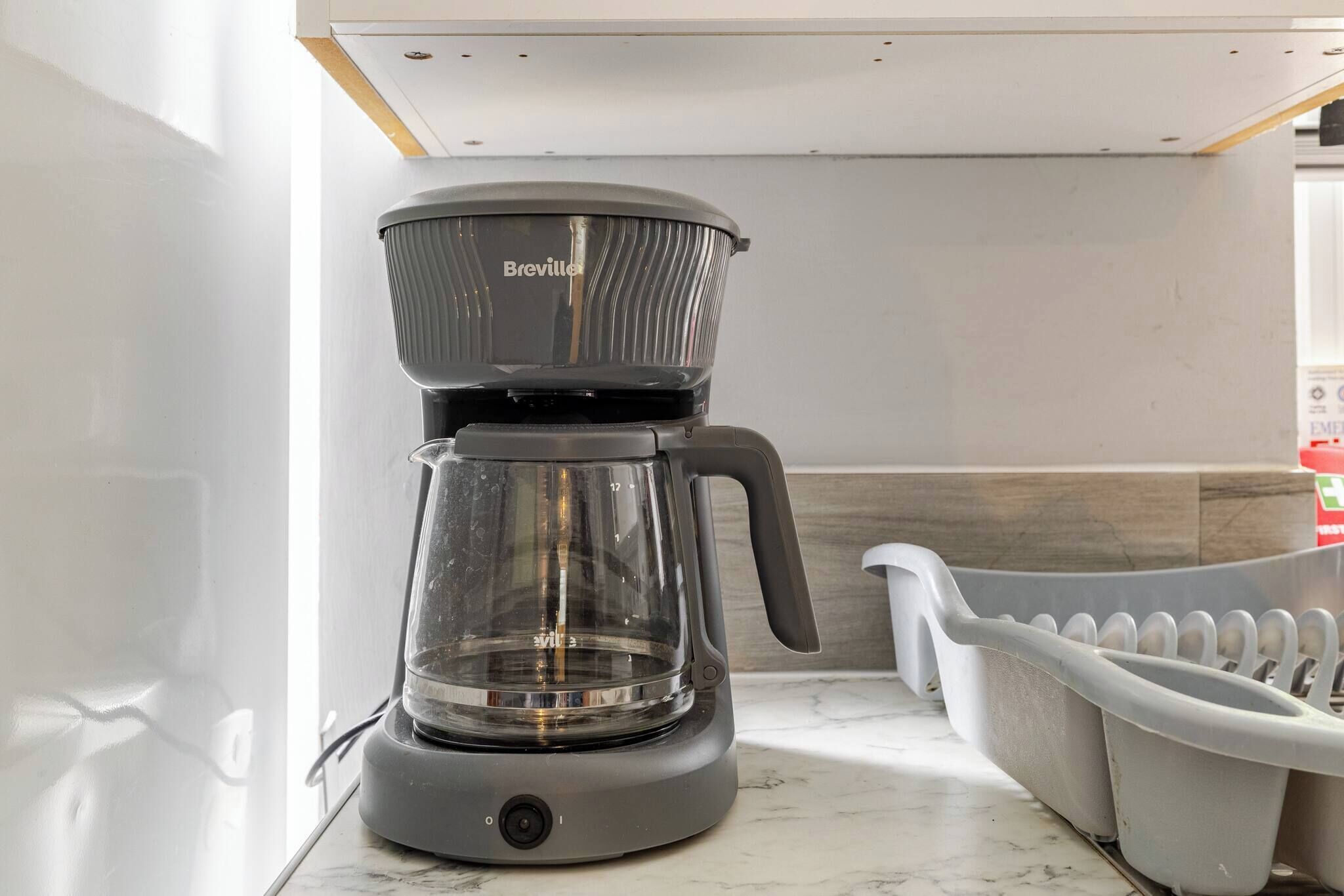 Een Breville koffiezetapparaat op een aanrecht in een keuken, met een witte spoelbak en een houten blad.