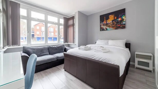 Una habitación de hotel moderna con una cama grande, un sofá, un escritorio y un ventanal con vistas a la ciudad.