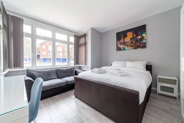 A modern hotel room with a large bed, a sofa, a desk, and a window with a city view.