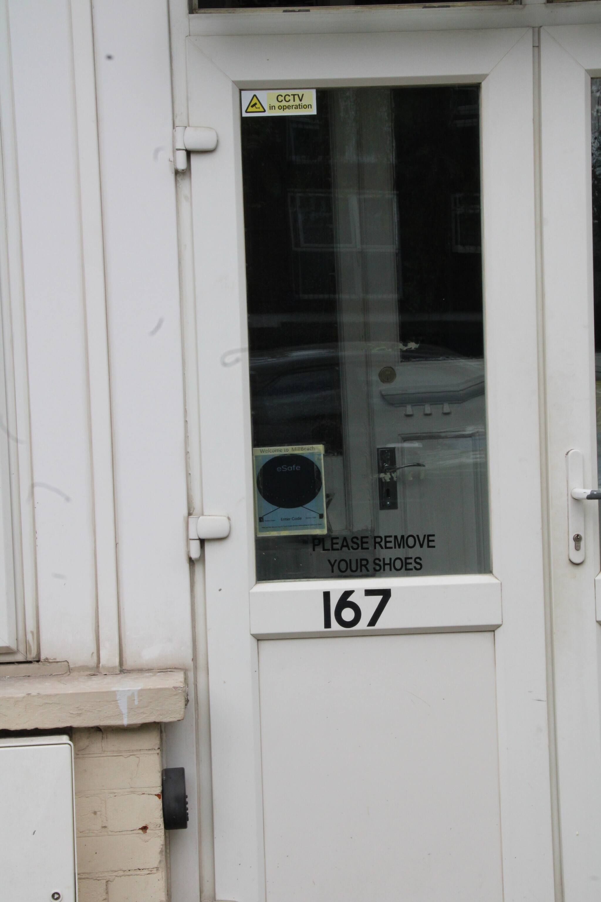 A door with a CCTV warning sign, a shoe removal sign, and the number 167.