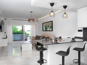 A modern kitchen with a central island, bar stools, pendant lighting, and a large window with a view of greenery. - Ca Maestral by Interhome (Marbella)