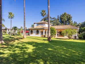 Una casa de dos plantas con techo de tejas, rodeada por un césped cuidado y palmeras.