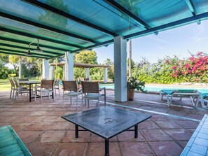 Eine überdachte Terrasse mit Billardtisch, Sitzgelegenheit im Freien und Blick auf einen Swimmingpool.