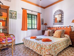 Quarto com cama, uma cadeira, janela com cortinas, espelho e piso estampado.