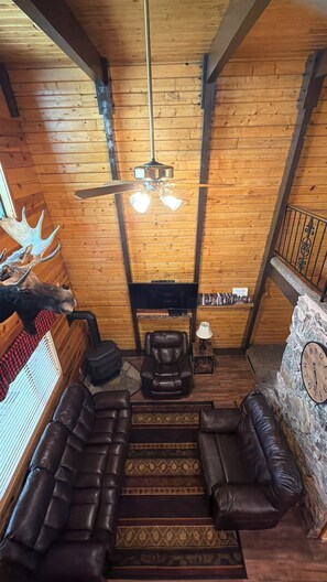 A log cabin interior with a ceiling fan, leather sofas, a fireplace, and a mounted moose head. - 20 min from Yellowstone NP, hot tub, sleeps 18, 3-bedroom, 2.5 bath, Island Park (Island Park)