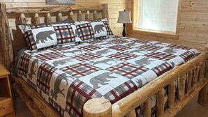 Ein Schlafzimmer einer Holzhütte mit Bett, Deckenventilator, Fenster mit Jalousien und einem Bild an der Wand.