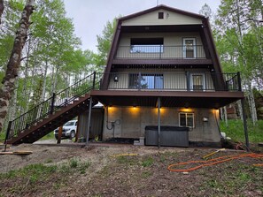 A two-story log cabin with a balcony, a staircase, and a covered outdoor area. - 20 min from Yellowstone NP, hot tub, sleeps 18, 3-bedroom, 2.5 bath, Island Park (Island Park)