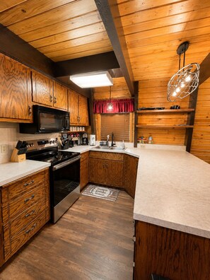A kitchen with wooden cabinets, a microwave, stove, and a sink. - Spacious Cozy Cabin. 20 to Yellowstone, hot tub, sleeps 18, 3-bedroom, 2.5 bath (Island Park)