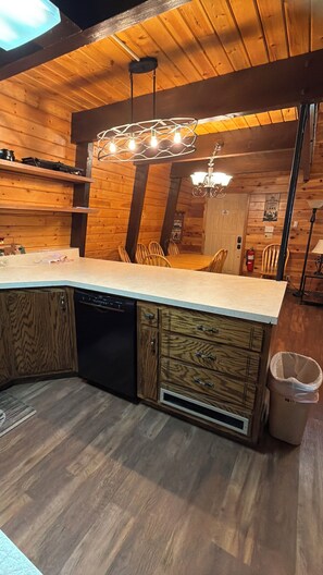 A kitchen with wooden cabinets, a dishwasher, a sink, and a dining area with chairs. - 20 min from Yellowstone NP, hot tub, sleeps 18, 3-bedroom, 2.5 bath, Island Park (Island Park)
