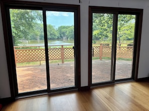 A room with a large sliding glass door leading to an outdoor deck with a wooden floor and a view of a lake and trees.